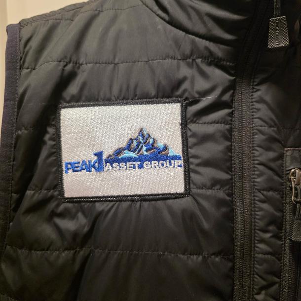 Completed black vest with an embroidered Peak Asset Group logo patch